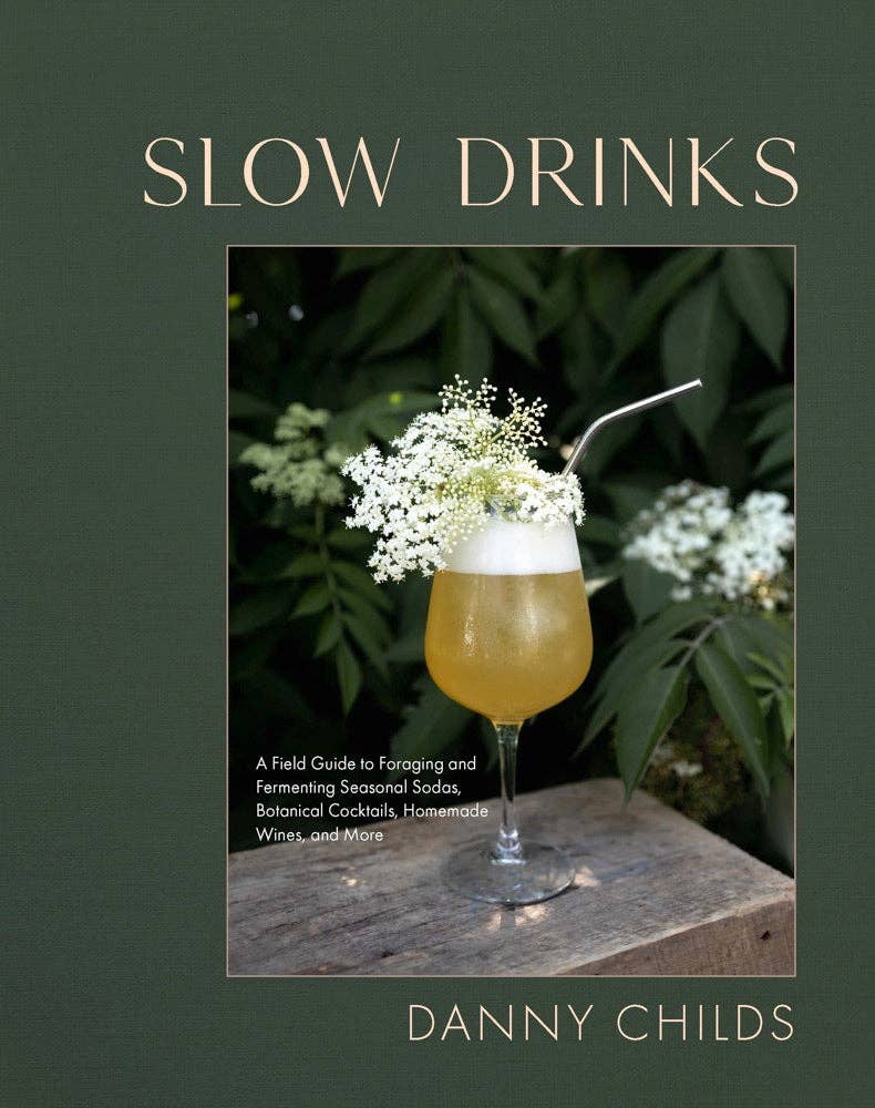 The cover of the book 'Slow Drinks' by Danny Childs featuring a photograph of a cocktail garnished with a white flower on a wooden surface, with greenery in the background.